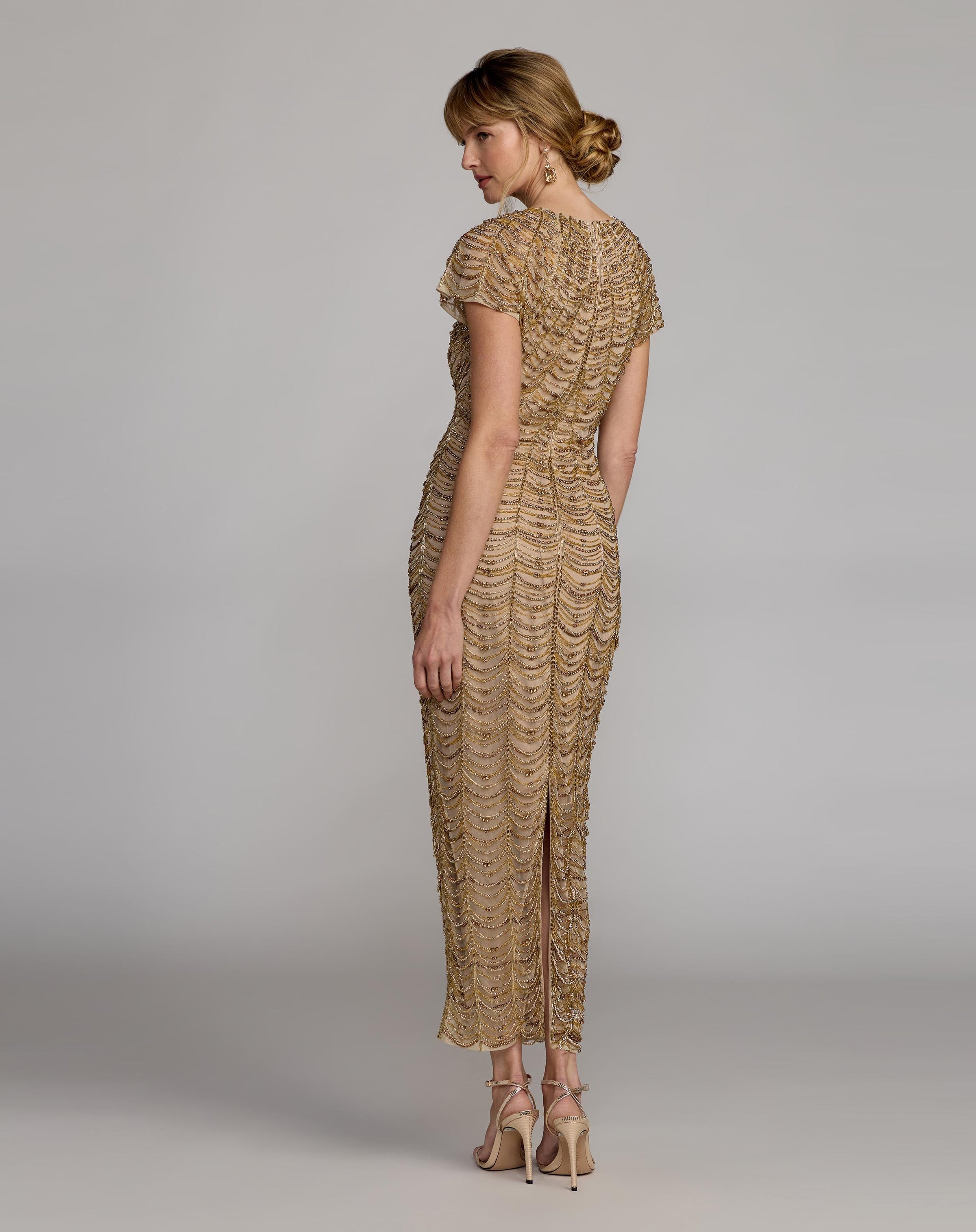 Woman wearing a gold lace dress against a gray background