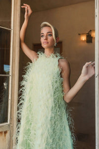 Editorial lifestyle shot of a model wearing the high-neck feather gown in Mint, capturing the movement of the high-low skirt.