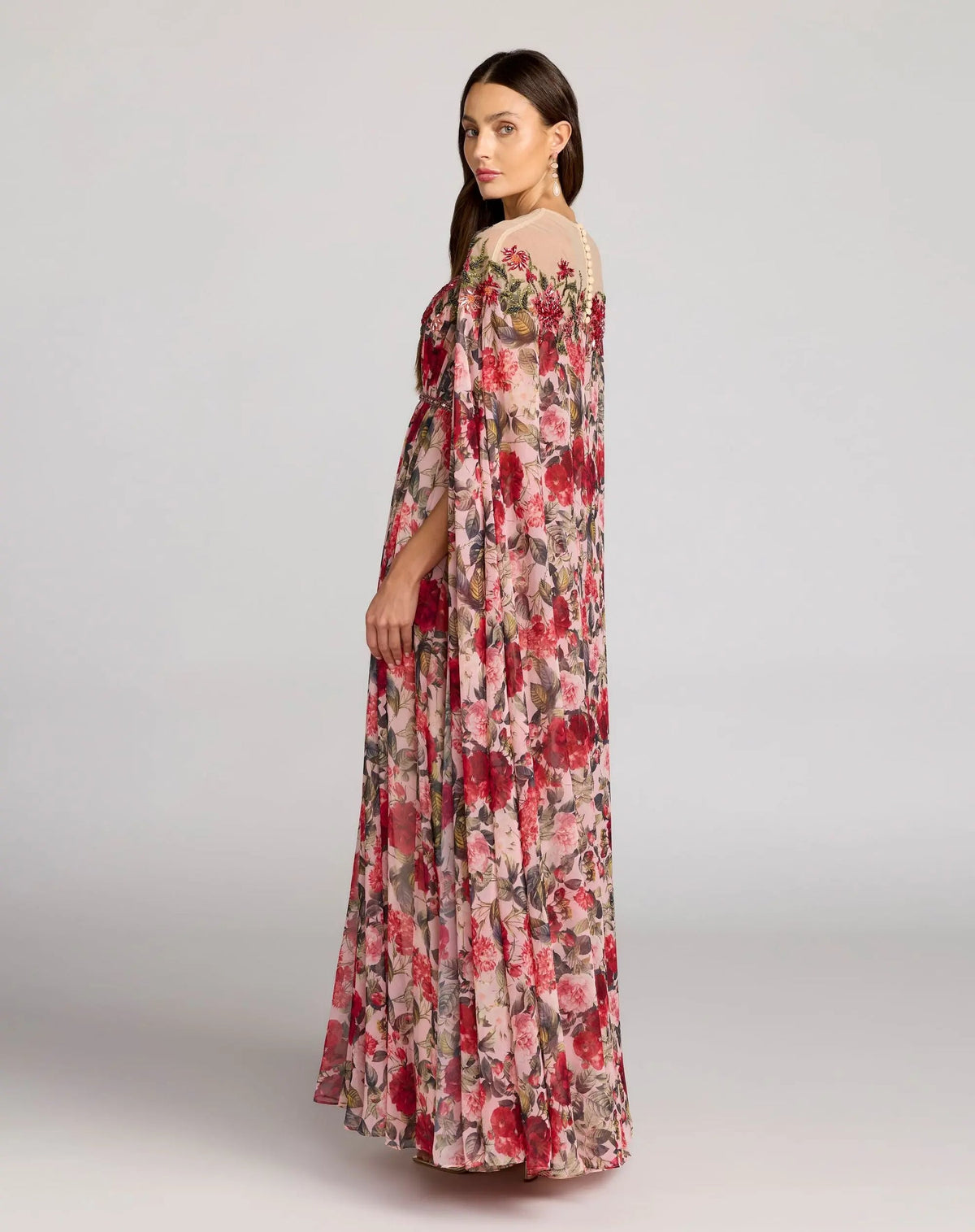 Rear view of the floral chiffon gown showing the dramatic cape movement and button back closure.