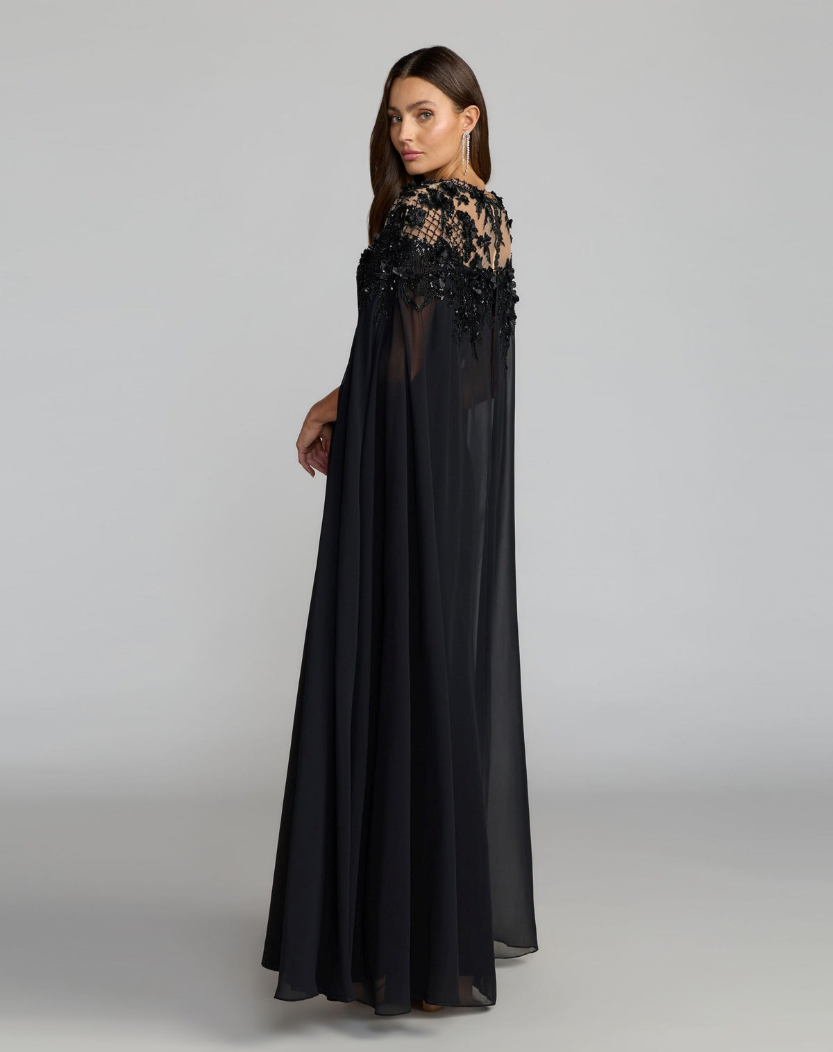 Side profile view of Mac Duggal 11954 black crepe gown featuring sheer chiffon cape sleeves and embroidered bodice details