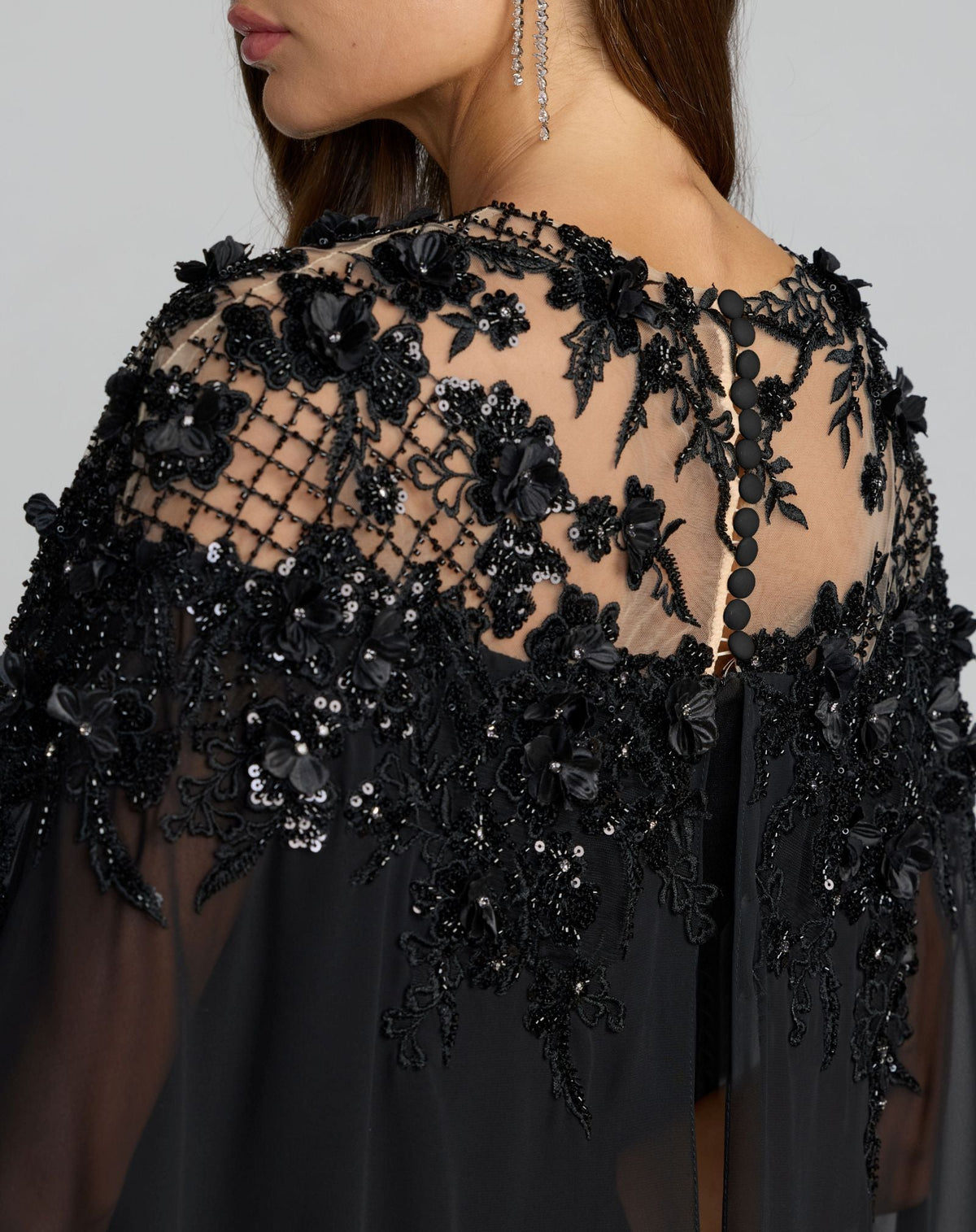 Close-up back view of Mac Duggal 11954 black gown showing button closure, embroidered bodice, and sheer cape sleeve construction