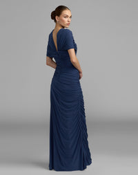 Back view of a model in a sapphire jersey gown showing the V-back and allover ruched detailing.