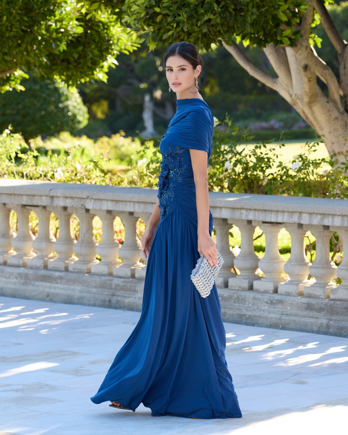 Full-length view of a model walking in a sapphire ruched jersey gown.