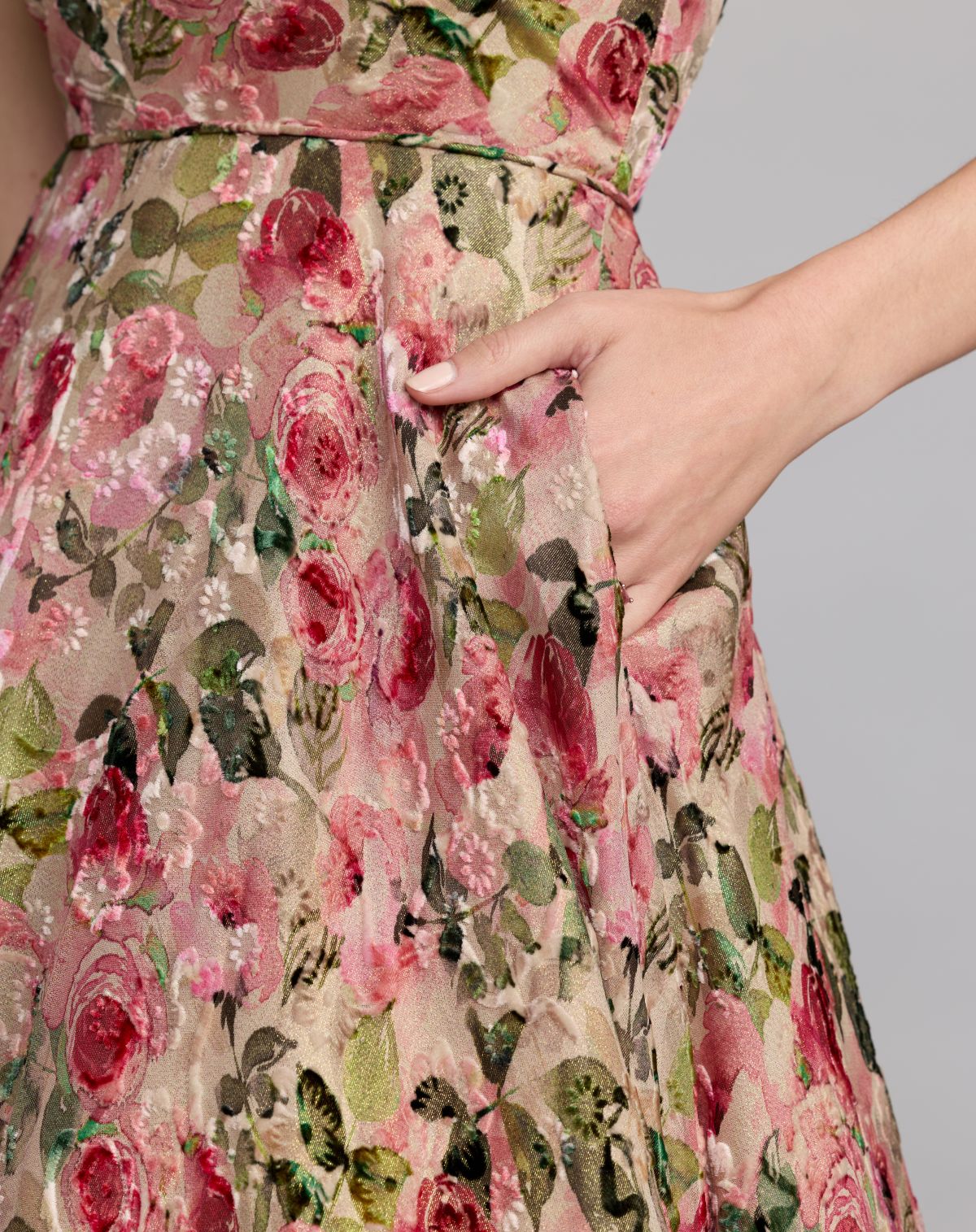 Floral dress with a hand adjusting the waistband against a gray background