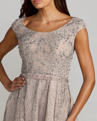 A close-up of a woman wearing a light blush pink dress with intricate silver beaded embroidery and a matching beaded waistband, set against a solid gray background.