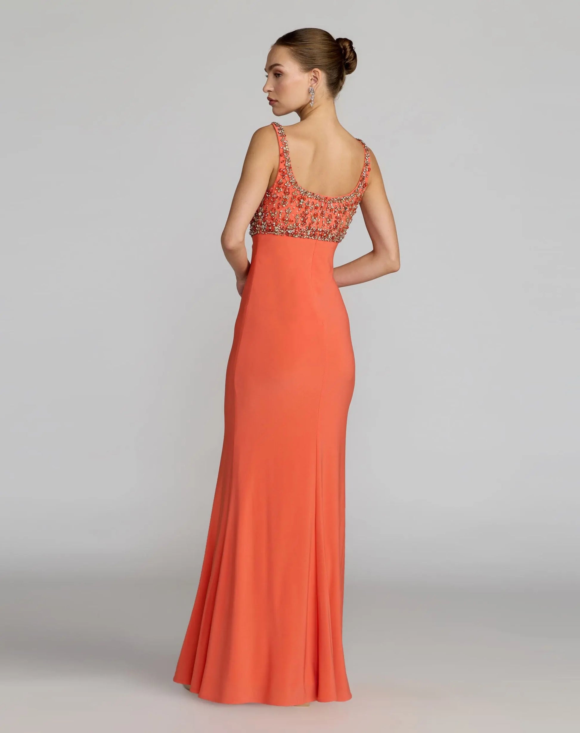 Woman wearing an orange evening gown with a beaded neckline on a plain background