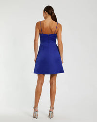 A woman shown from the back wearing a bright royal blue mini dress with thin straps and a fitted silhouette, paired with metallic high-heeled sandals, against a plain light gray studio background.