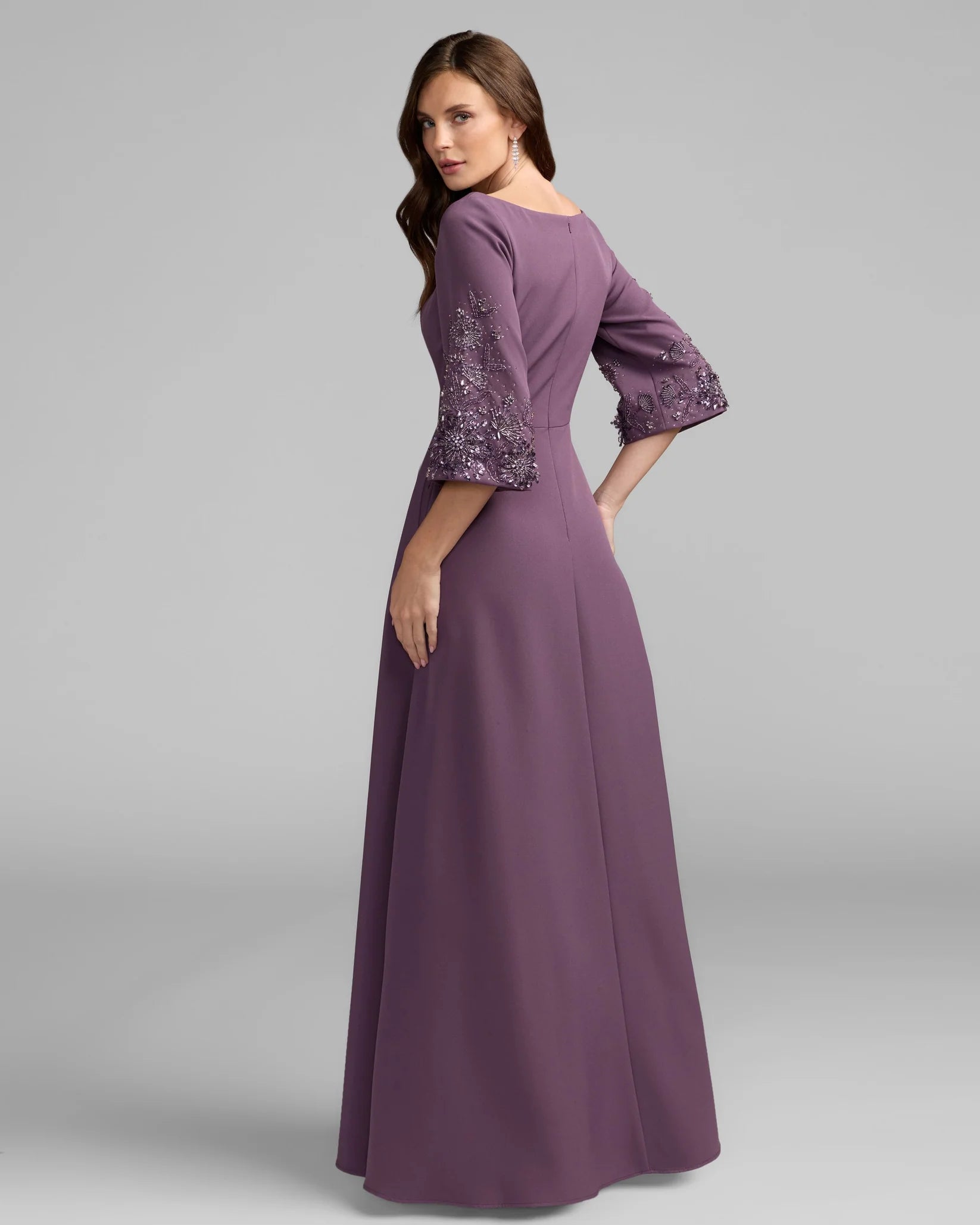 Woman wearing a long purple dress with lace detailing on a gray background