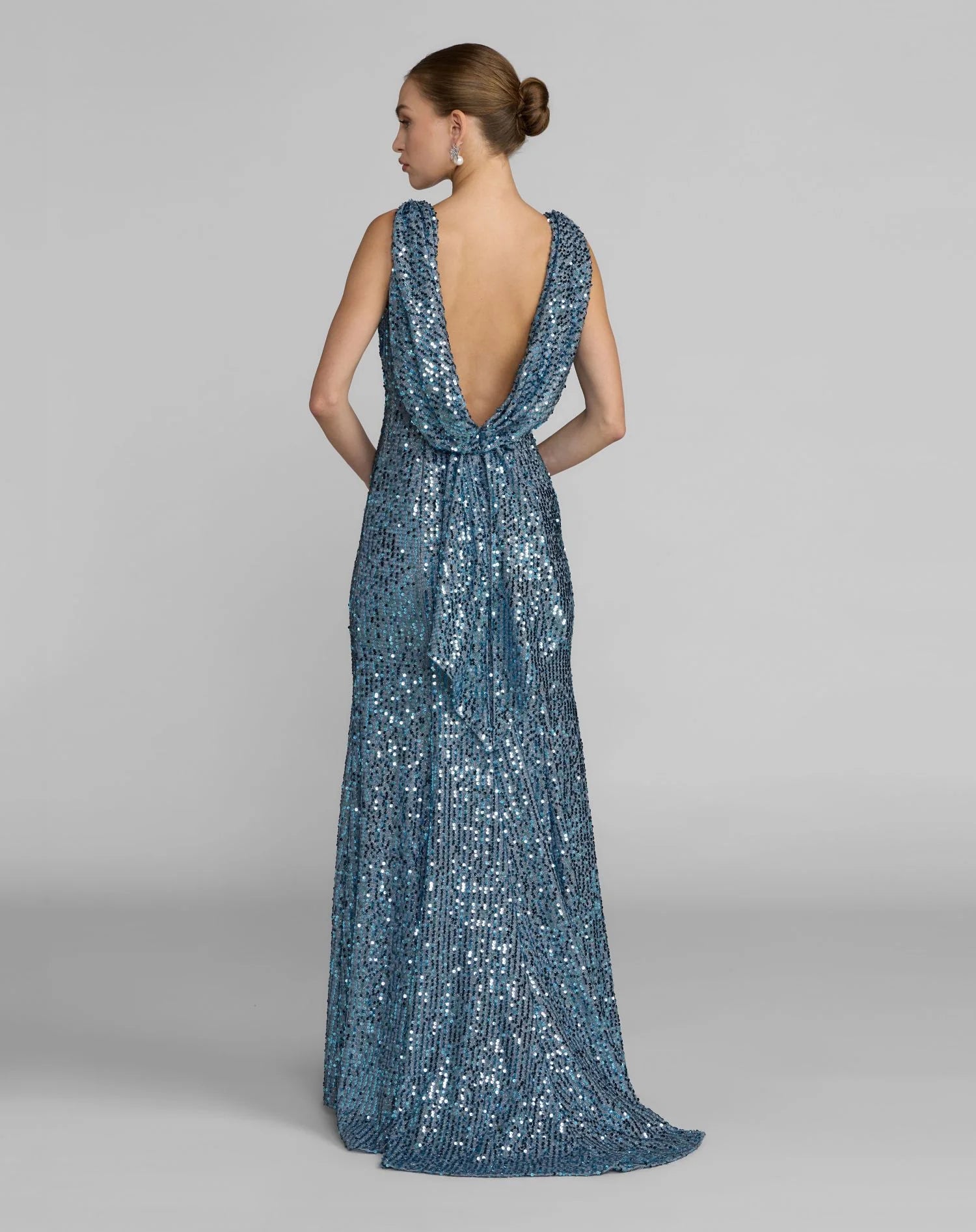 Woman wearing a blue sequin gown with a backless design on a gray background