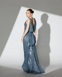 Woman in a blue sequin gown standing against a white background with a spotlight effect.