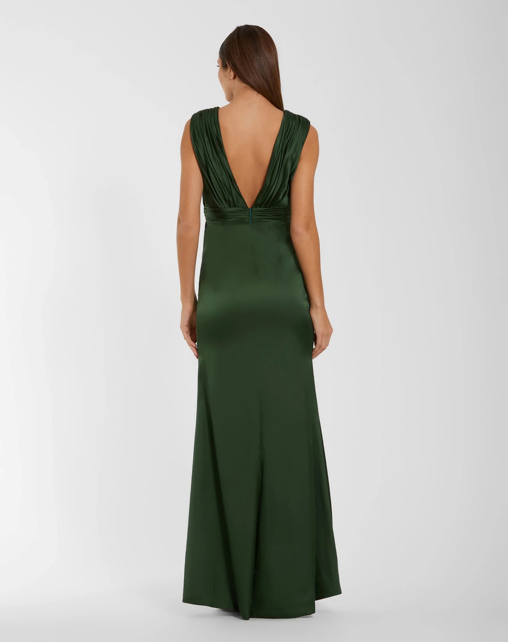 A woman wearing a floor-length dark green satin gown, shown from the back against a light gray studio background.