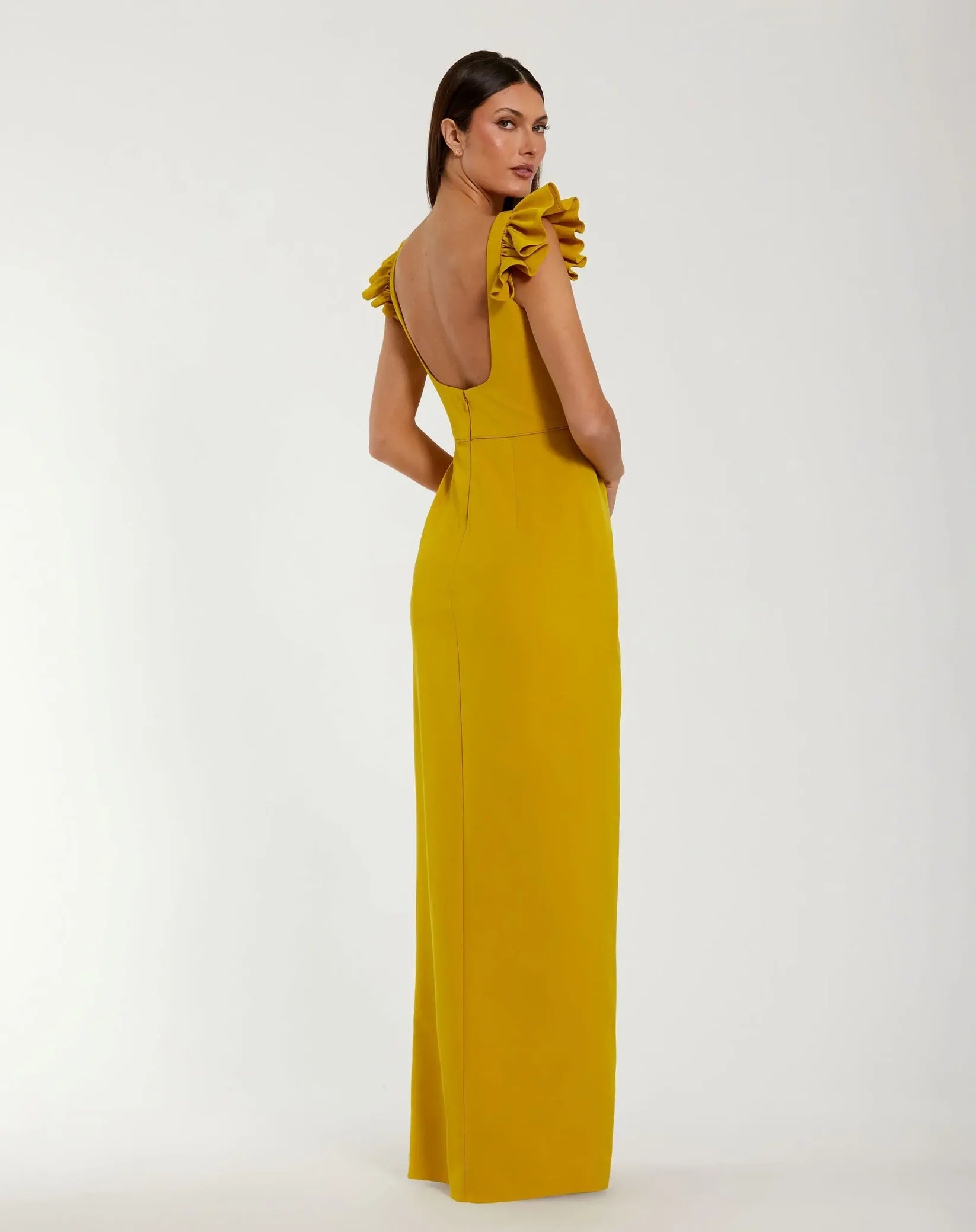 Woman wearing a mustard yellow dress with ruffled shoulders on a white background