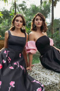Two models posing in a lifestyle shot, one wearing a black sleeveless gown with square neckline and floral embroidery, style 37149, 