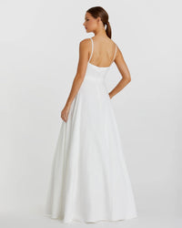 A woman modeling a white A-line wedding dress from the back, showing thin spaghetti straps, a low open back, and a flowing skirt against a light gray studio background.