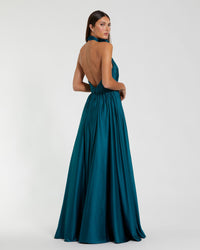 A woman modeling a floor-length teal green formal gown from the back, showing an open back and halter-style neckline, against a plain light gray studio background.