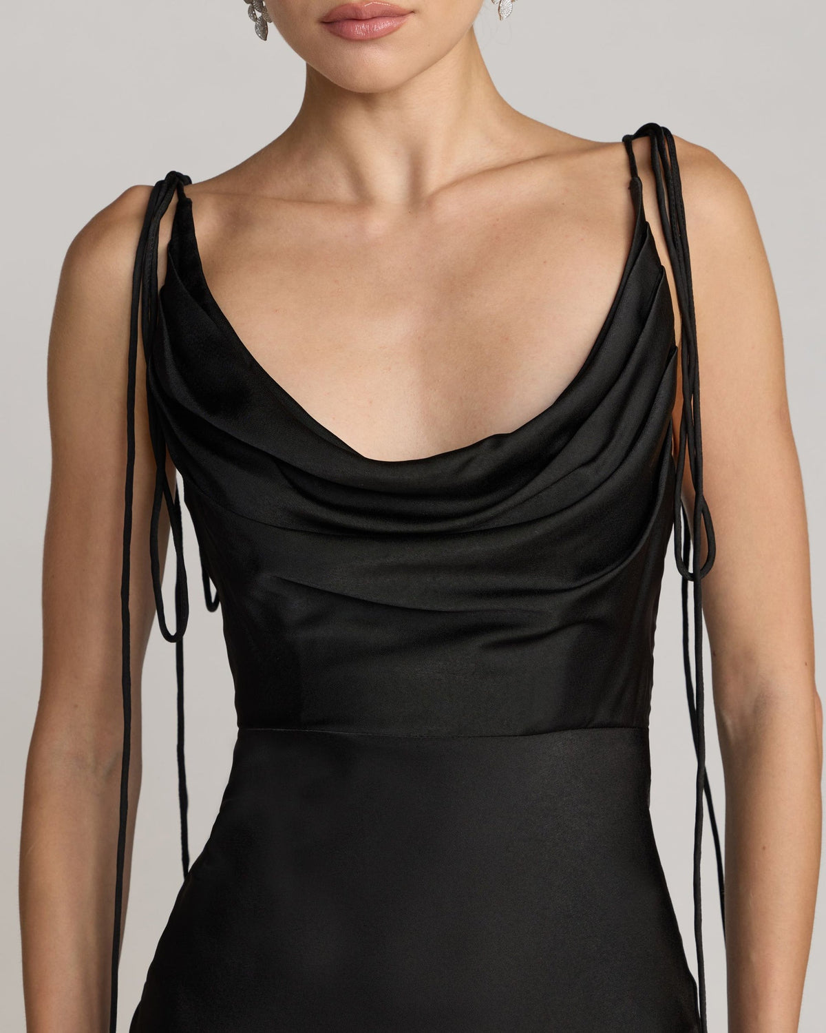 Close-up studio shot focusing on the liquid drape of the black charmeuse fabric across the cowl neckline and the delicate tie-strap detailing.