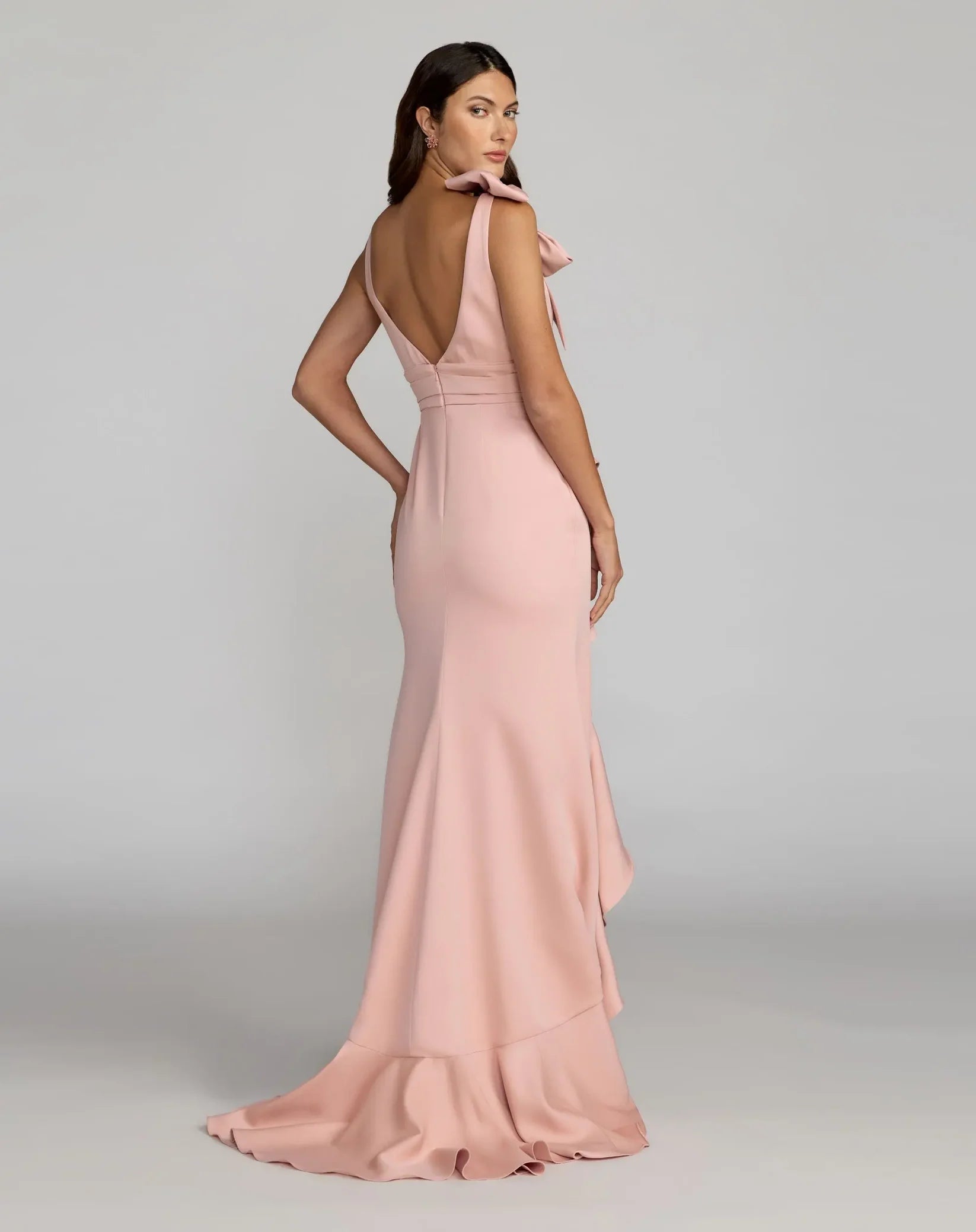 Woman wearing a pink evening gown with a backless design on a gray background