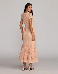 A woman modeling a peach lace maxi dress from the back, featuring short flutter sleeves, a fitted silhouette, and a flared lace-hem skirt, paired with black and white high heels against a light gray studio background.