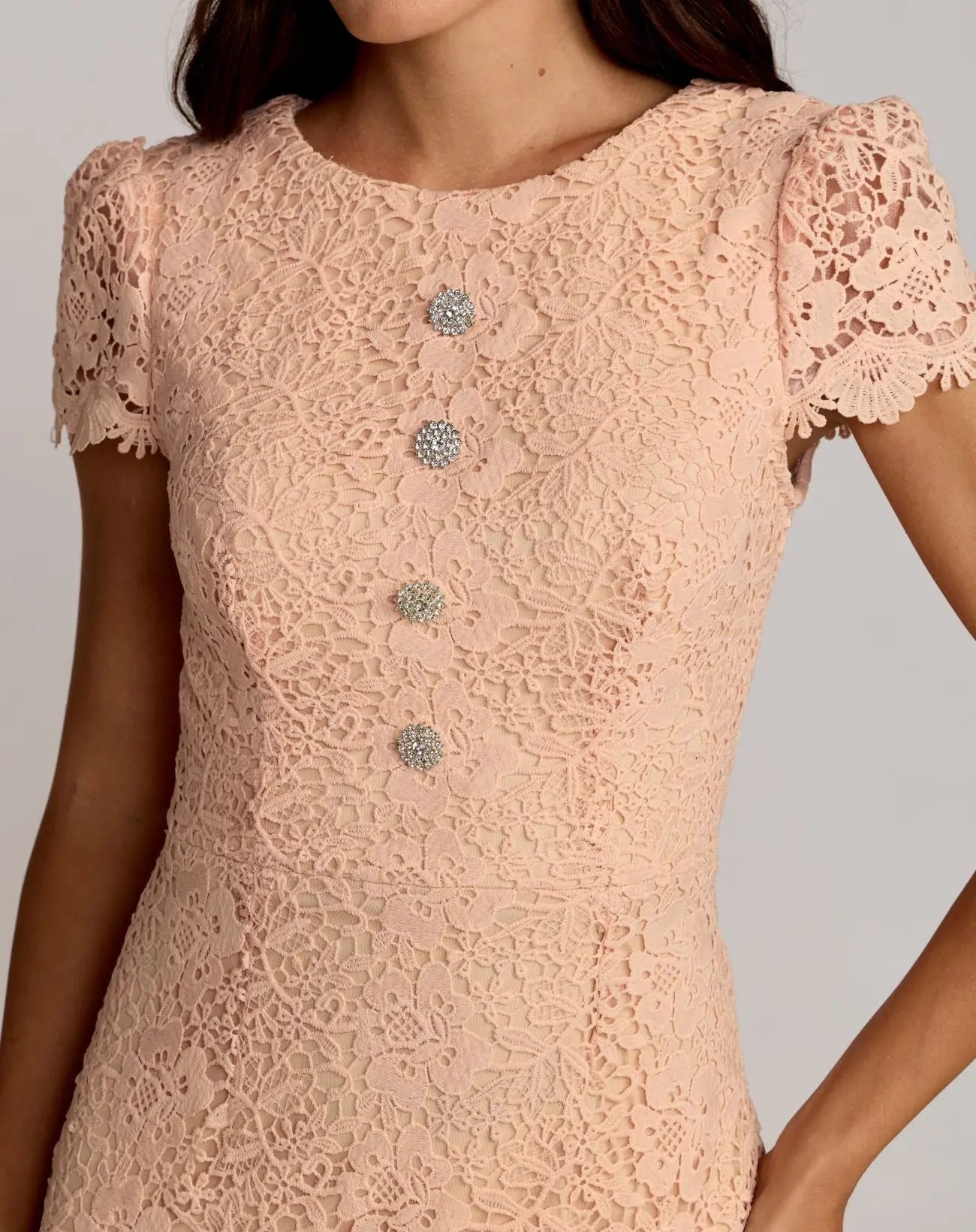 Pink lace dress with decorative buttons on a neutral background