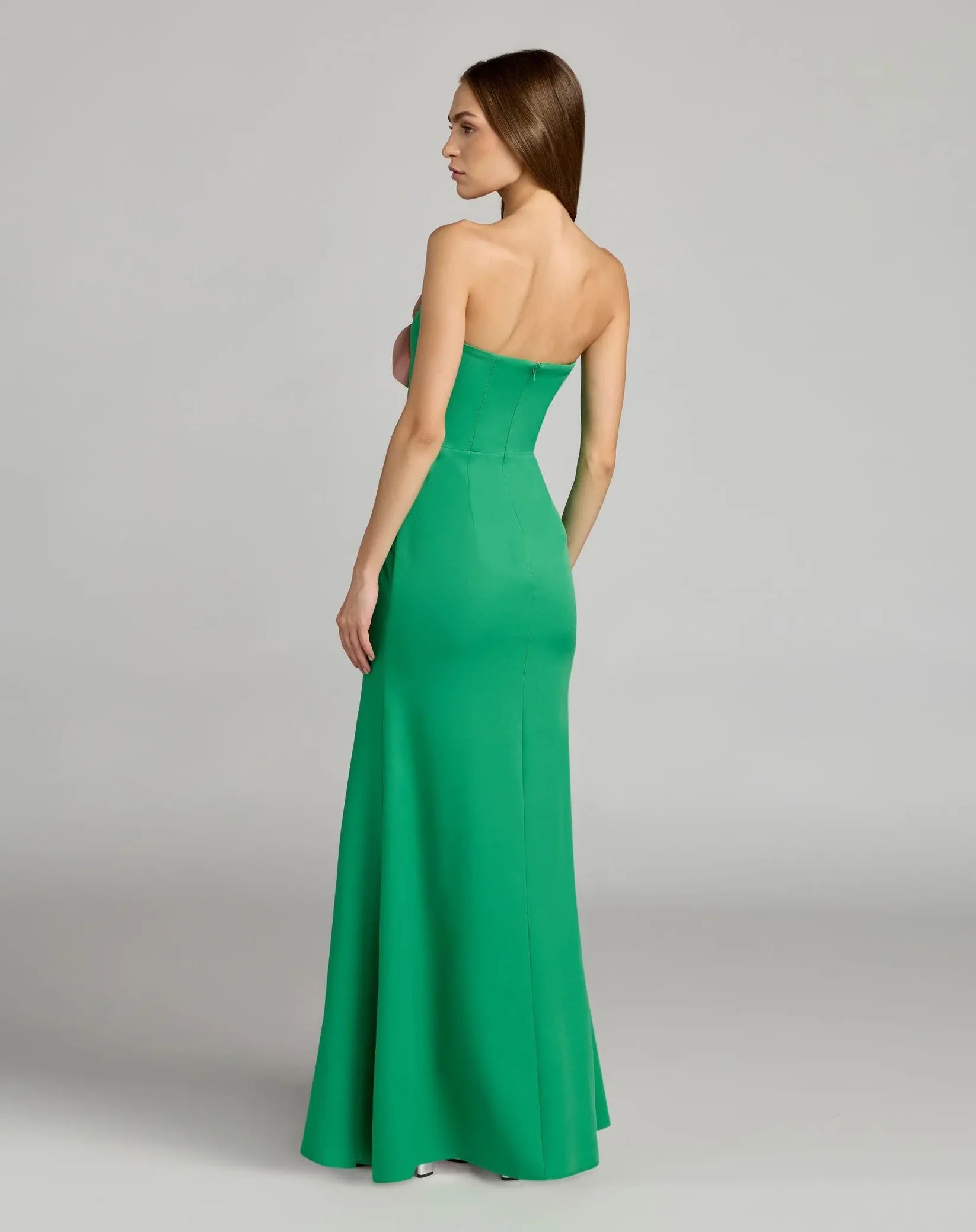Woman wearing a strapless green evening gown on a gray background