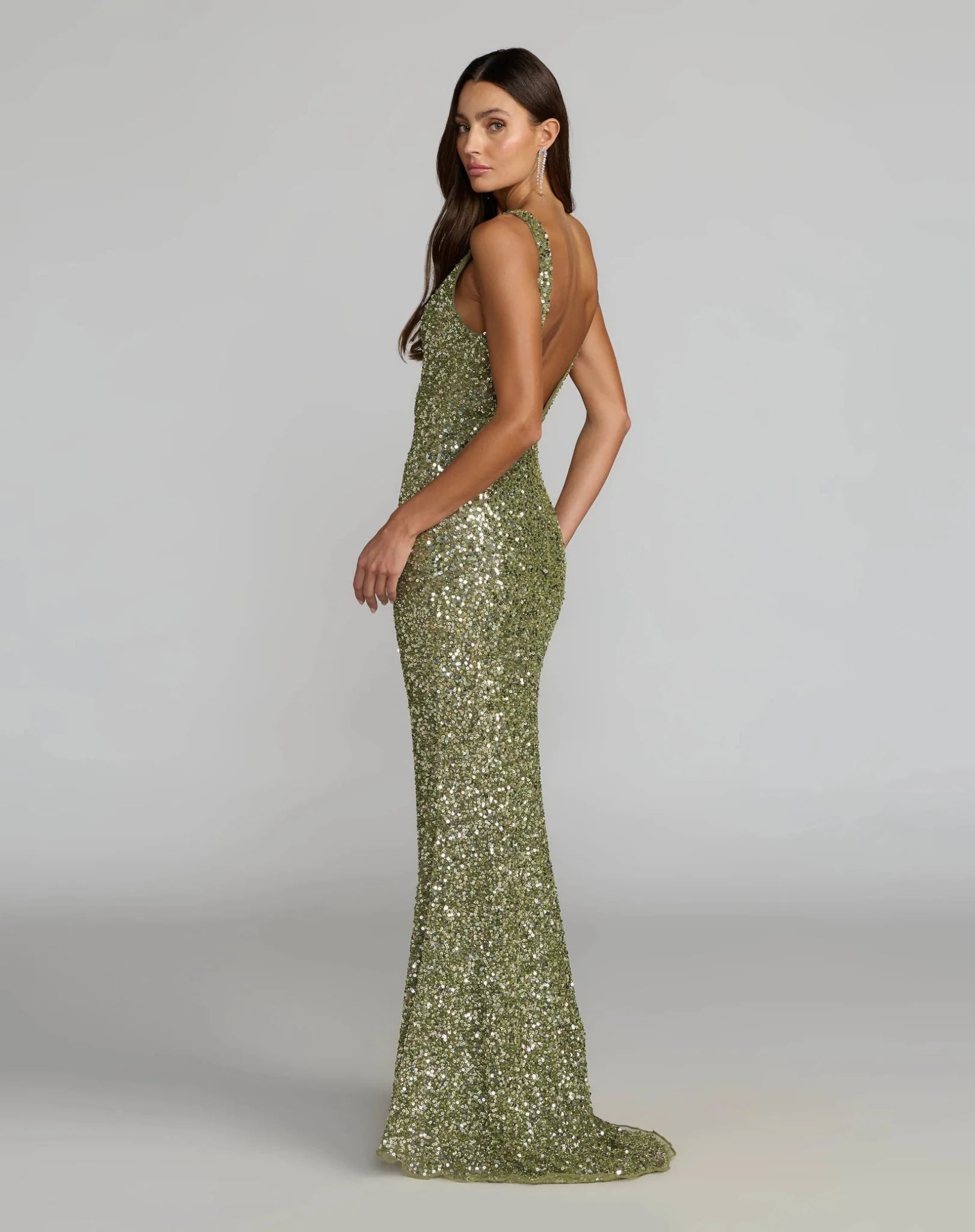 A woman modeling a floor-length olive green sequined gown with a halter neckline and backless open back, photographed against a light gray studio background.