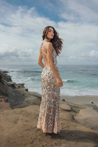 Woman in a silver backless sparkling dress standing on a rocky beach with ocean and sky in the background