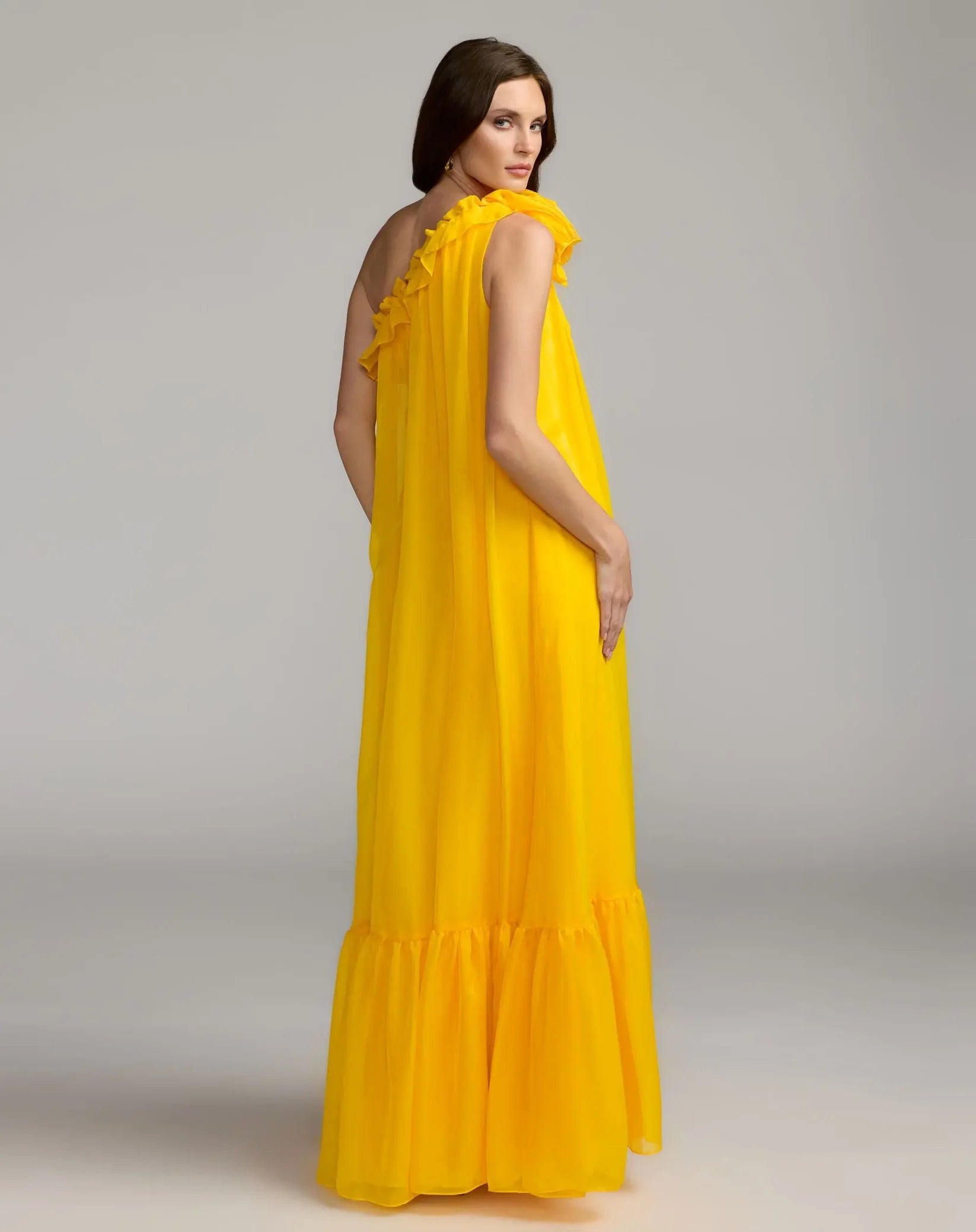 Woman wearing a yellow one-shoulder dress against a gray background
