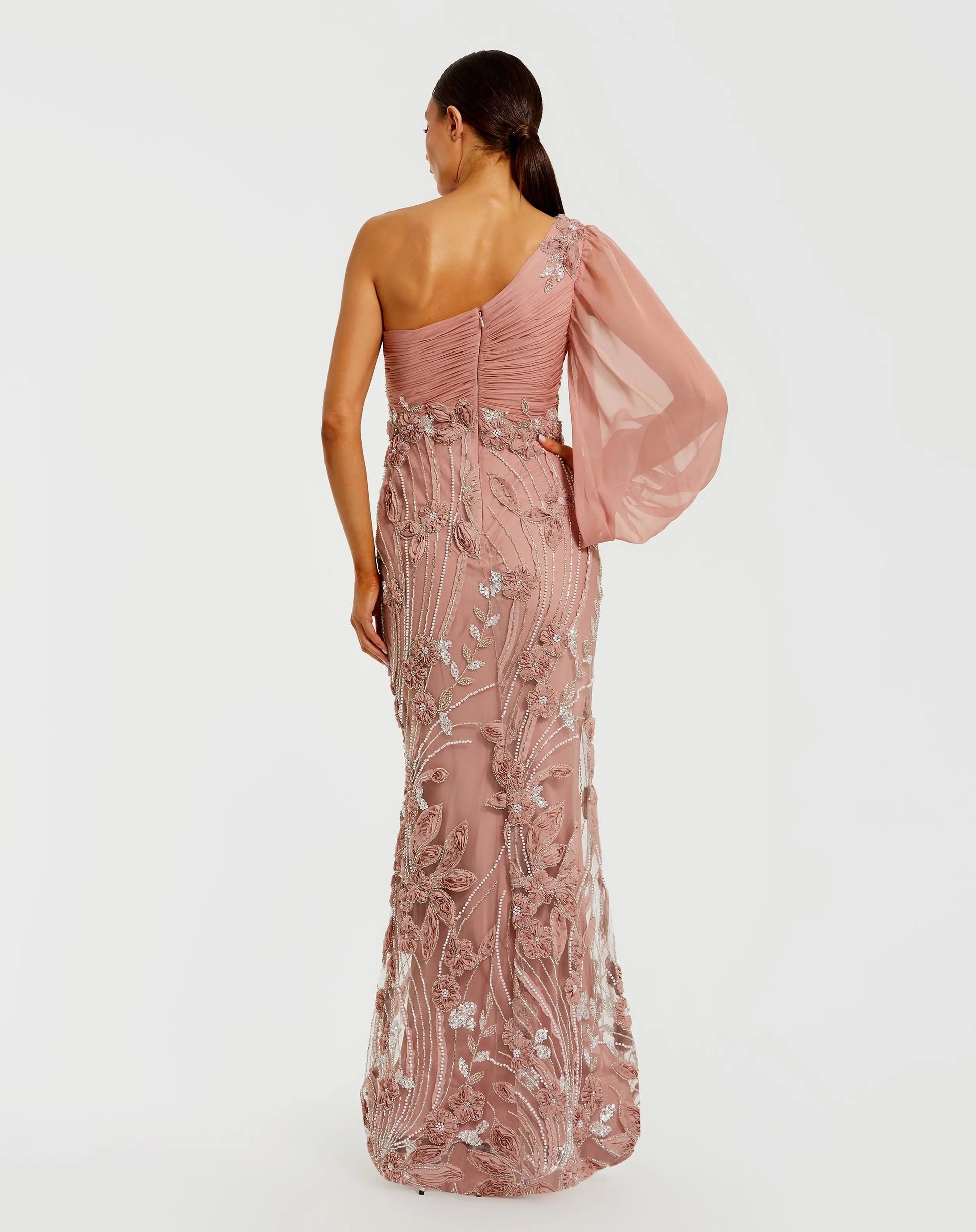 Woman wearing a pink one-shoulder gown with floral embroidery on a white background
