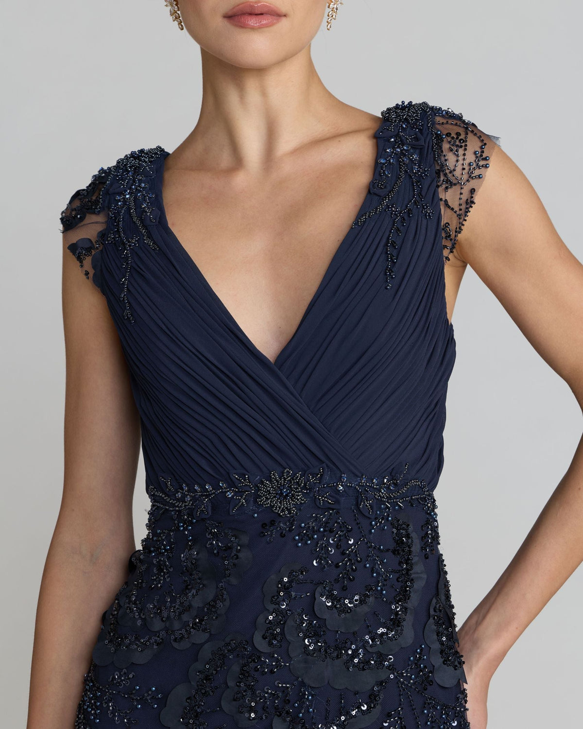 Close-up view of the ruched chiffon bodice and embellished cap sleeves on a midnight evening gown.