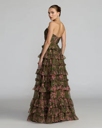 A woman modeling a strapless, floor-length gown with a tiered ruffled skirt. The dress features an olive green base with a pink floral pattern, shown from a three-quarter back angle against a light gray studio background.