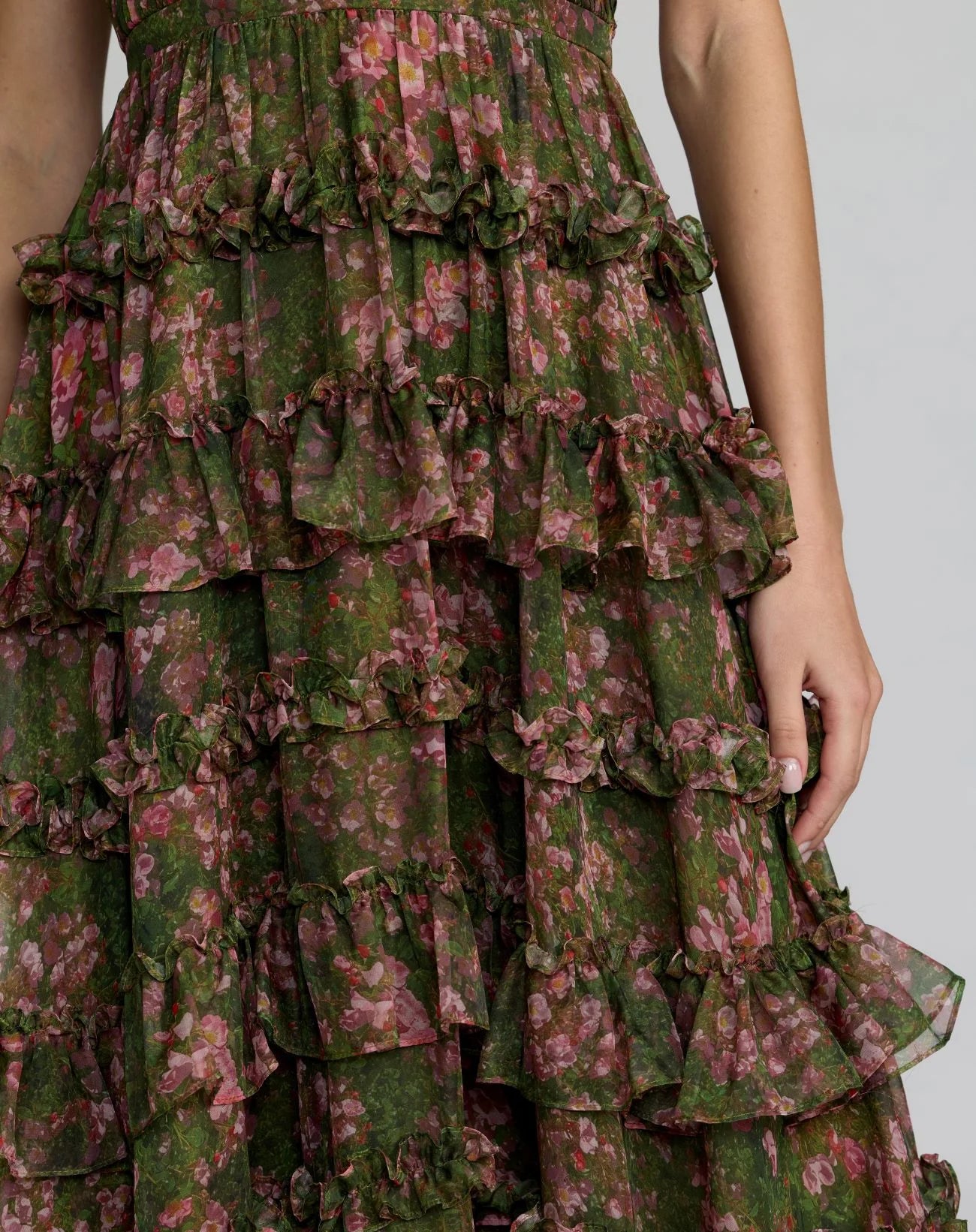 A close-up of a tiered ruffle skirt with a green and pink floral pattern, worn by a model against a light gray background.