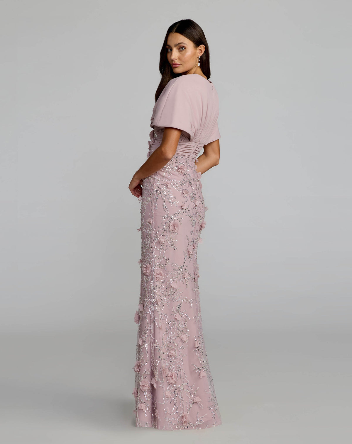 Back view of a model in a rose fitted gown, showing the cape sleeves and floor-length hem.