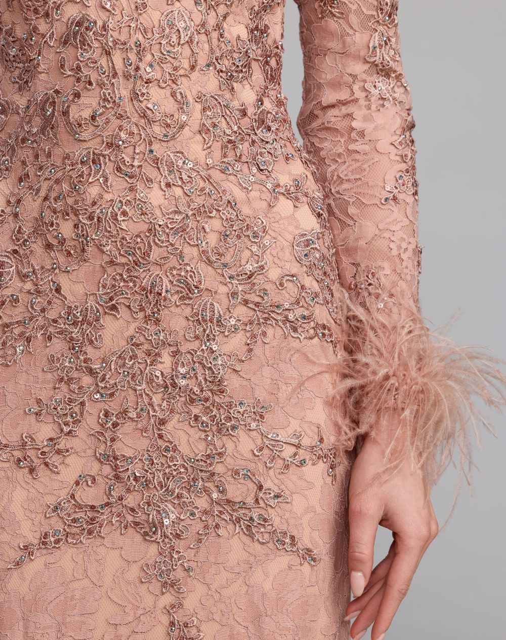 Close-up of a pink lace dress with intricate detailing and feathered sleeves on a gray background.