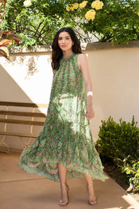 Woman in a green floral dress standing outdoors with greenery in the background