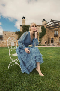 Woman in a blue dress sitting on a chair in front of a castle-like building.