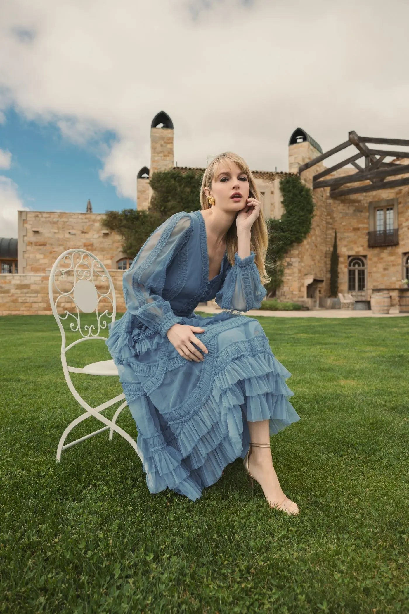 Woman in a blue dress sitting on a chair in front of a castle-like building.