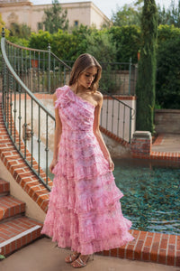 Woman in a pink one-shoulder dress standing by a poolside.