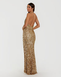 A woman modeling a floor-length, backless gold sequin gown against a plain light gray studio background.