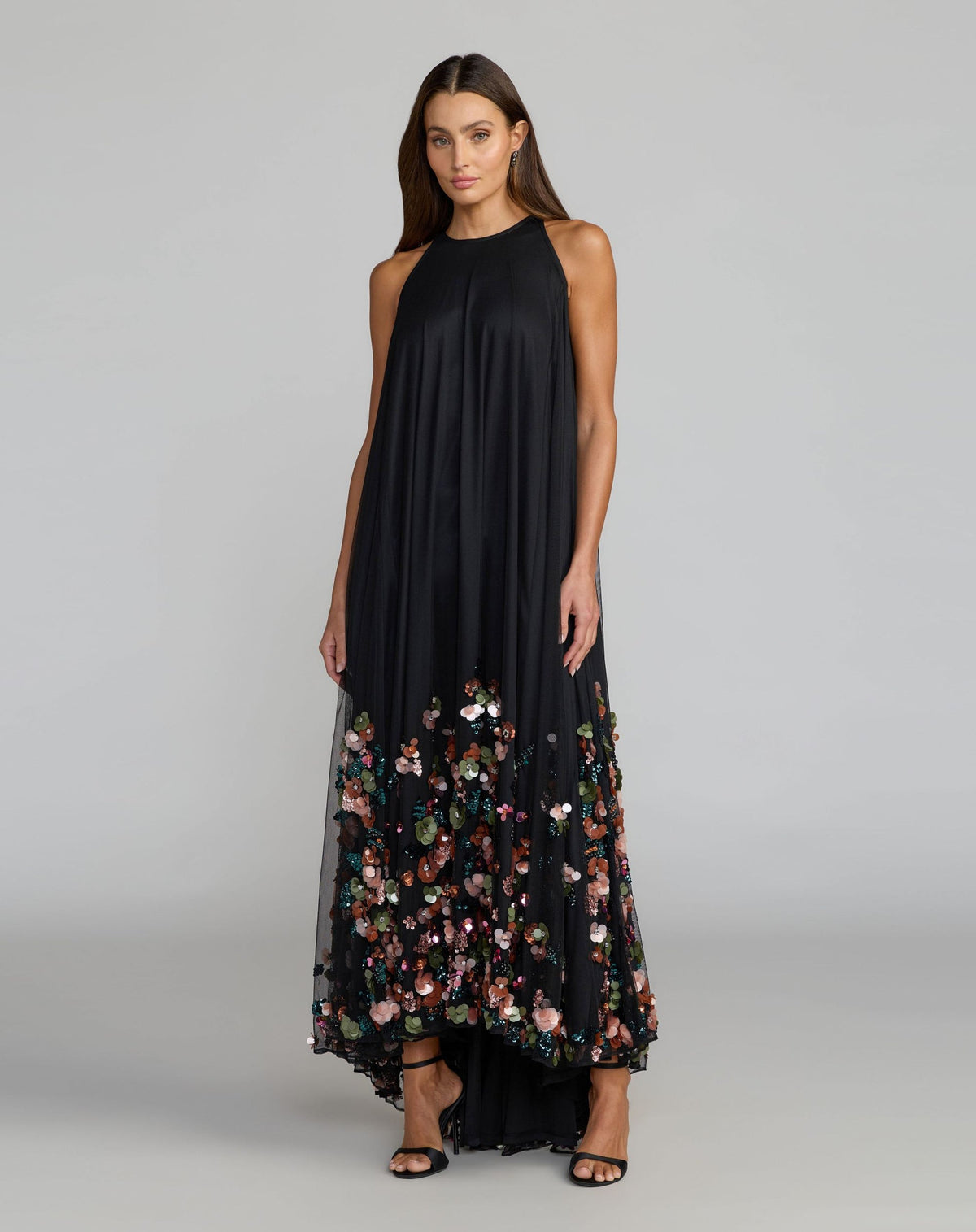 Model wearing Mac Duggal 94270 black floral sequin trapeze gown in a garden setting