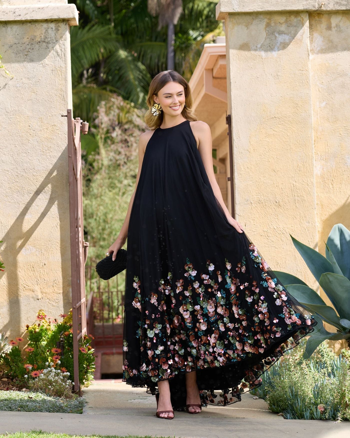 Model smiling in black sleeveless floral gown
