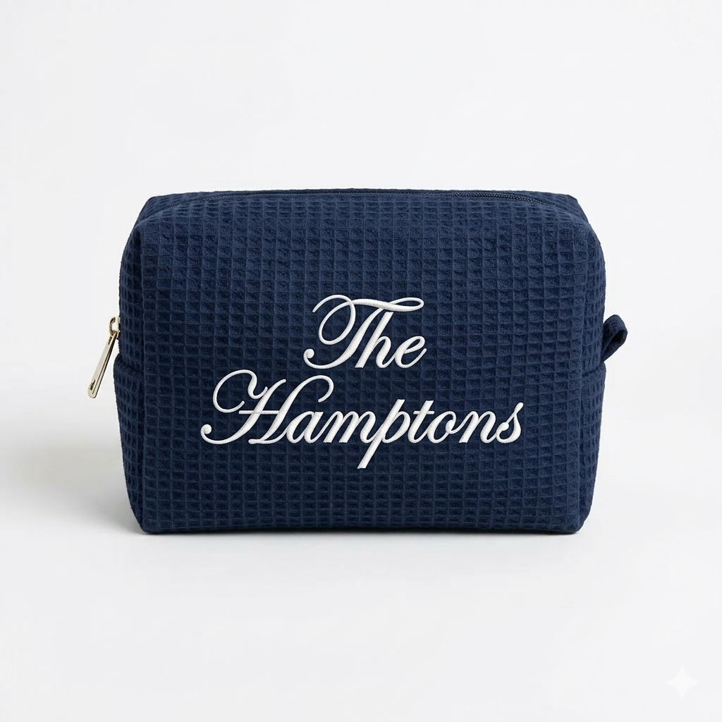 Navy blue waffle weave makeup bag with white 'The Hamptons' embroidery.