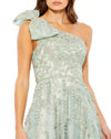 This incredible sage green gown is made from shimmery, botanical-embroidered tulle with with a rhinestone trim at the waist and topped with a feminine full bow at the single shoulder. It’s glamorous, romantic—and with a high leg slit—flirty, too. This gown is perfect for wedding guests and Summer parties close up