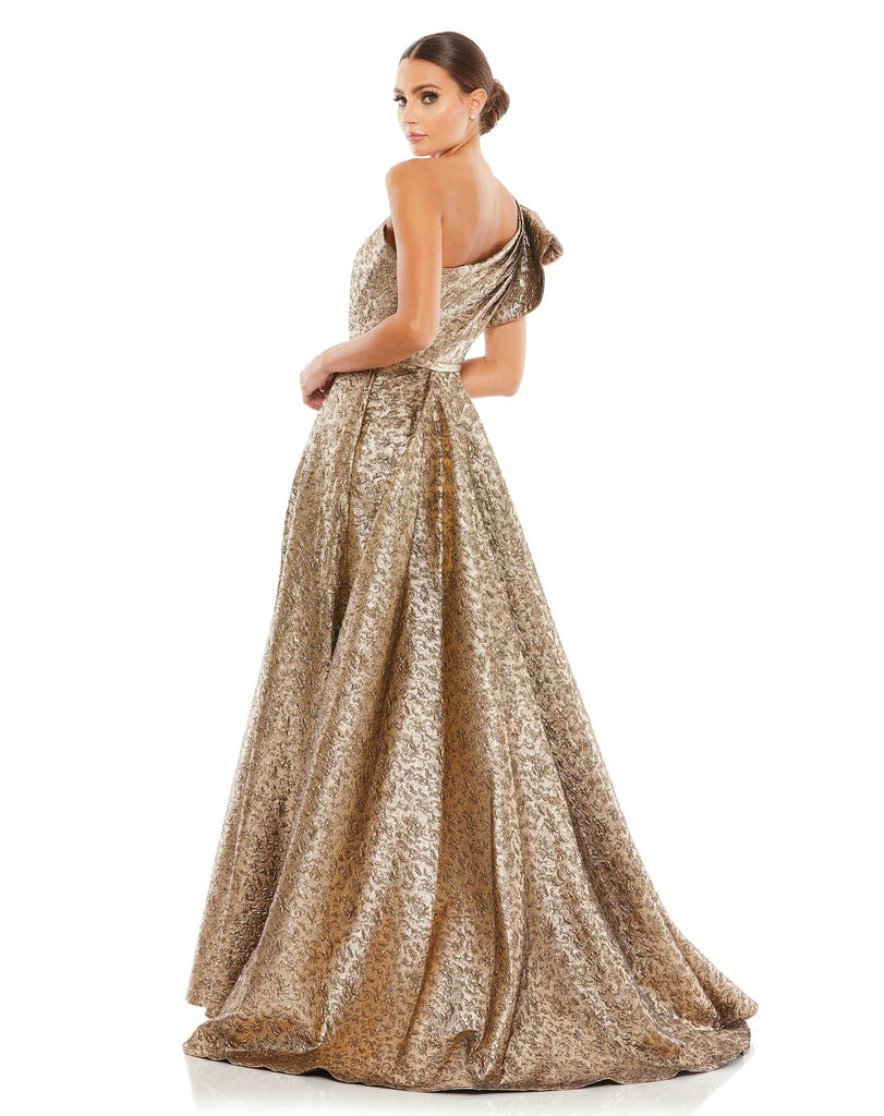 This stunningly elegant, one-shoulder metallic brocade antique gold, ball gown is a truly show-stopping evening dress accented with asymmetric chest detail, bow-detail on the shoulder, a cinched in waist and a beautiful full skirt with a thigh high split. This A line ball gown is perfect for proms, black-tie affairs, weddings and special events back view
